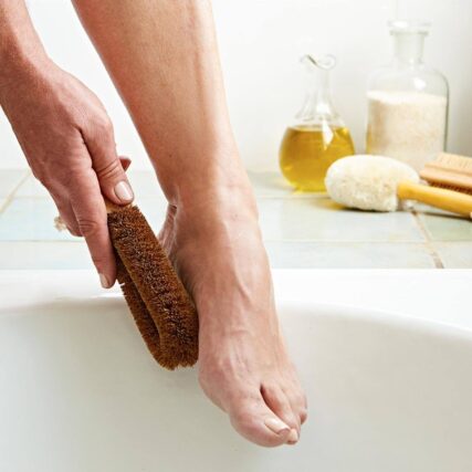 Ecomax foot brush scrubbing a foot in bathroom with ecomax face brush in background