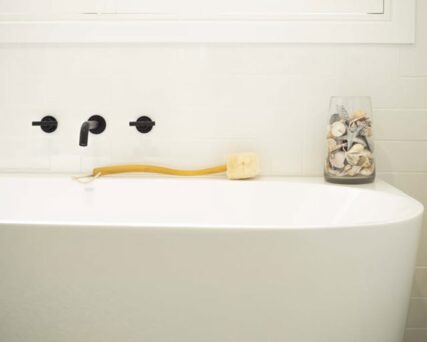 Ecomax body brush with handle sitting on the side of a bath tub.